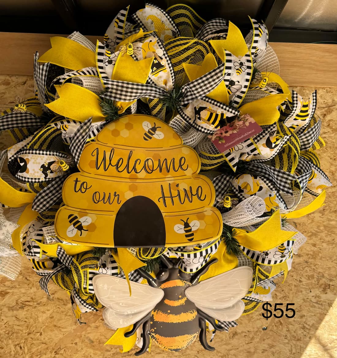 A spring wreath buzzing with charm: a plush bee at the center of yellow and white blooms with gingham ribbon.