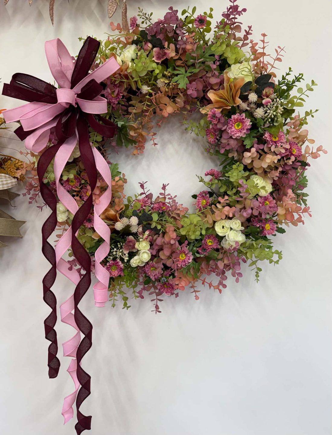 The same autumn eucalyptus wreath finished with a rose-pink and burgundy bow trailing long curled ribbon tails.