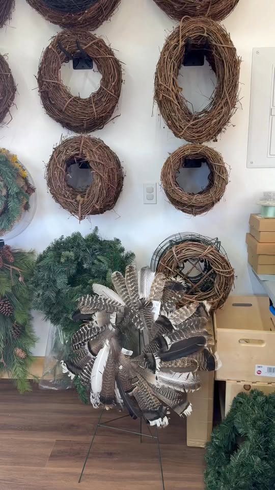 The workshop wall: bare grapevine bases hung and ready, evergreen stock below, and a feather wreath in progress.
