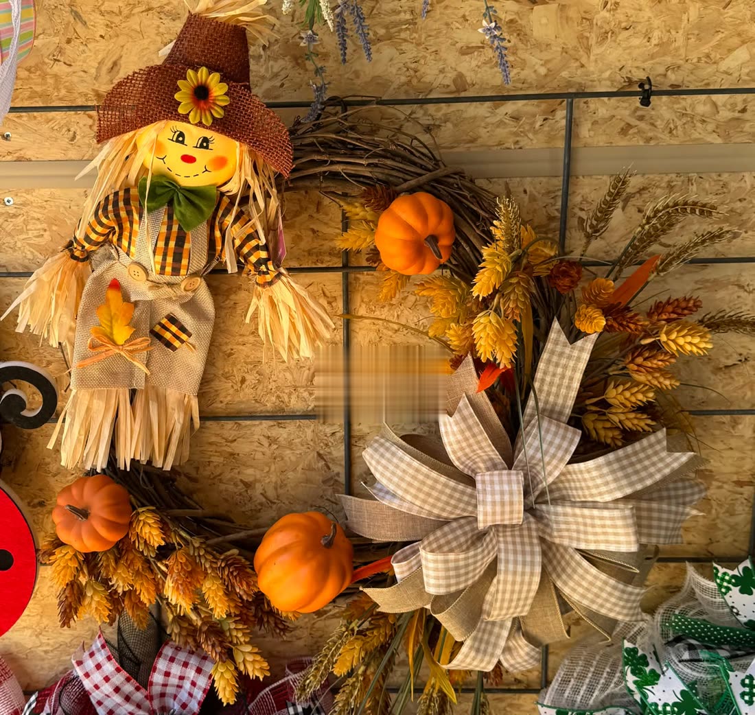 A smiling scarecrow tucked into a fall wreath with sunflowers, plaid ribbon, and harvest sprays.